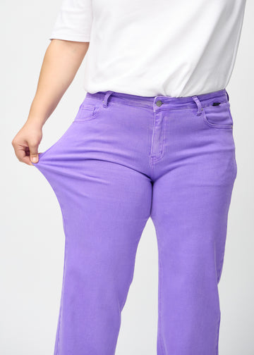 Plus-size model strækker jeansene ved låret for at vise stretch.