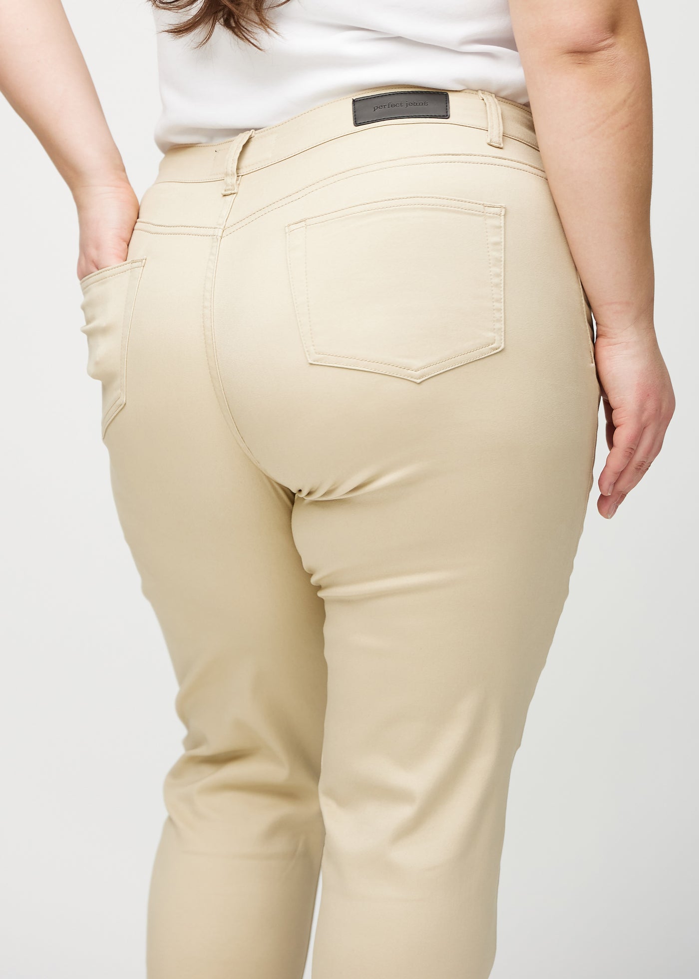 Beige slim jeans set bagfra tæt på en plus-size model for at vise detaljer.