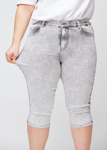 Plus-size model viser stretch ved at trække i caprisene ved låret – fokus på komfort og fleksibilitet i den lysegrå denim.