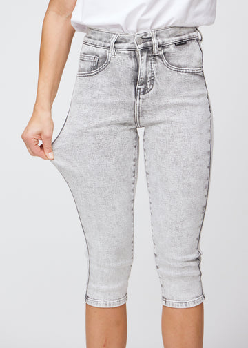 Model strækker caprisene ved låret for at vise det bløde og fleksible stretch i den lysegrå denim.