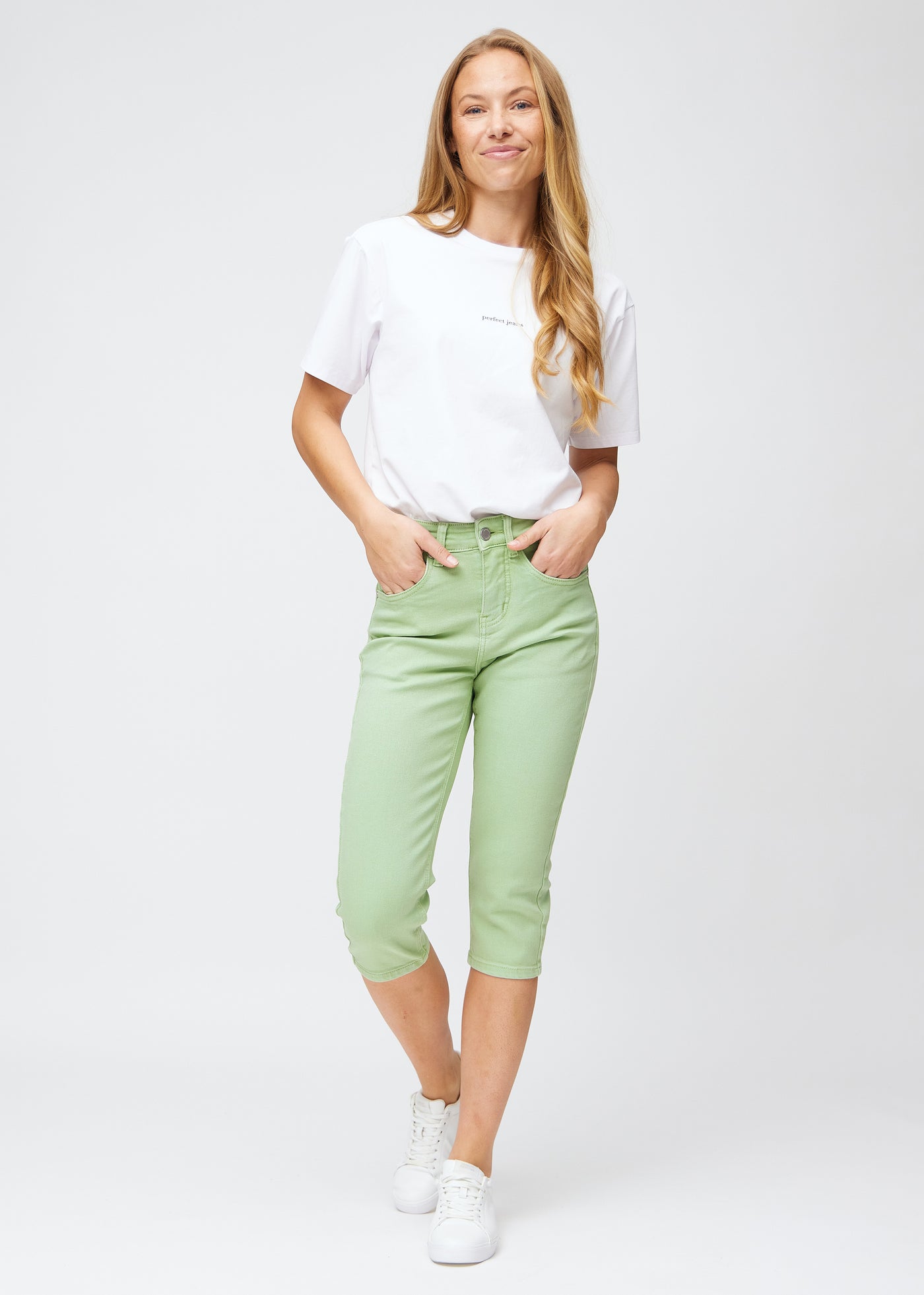 Model træder ind i billedet, strækker i sine lysegrønne slim capris, viser dem frem ved at dreje rundt, og går derefter ud af billedet igen.