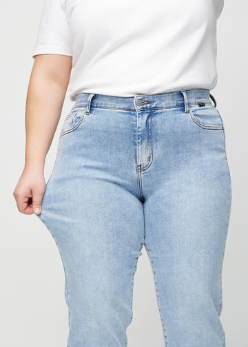 Plus-size model strækker jeansene ved låret for at vise stretch.