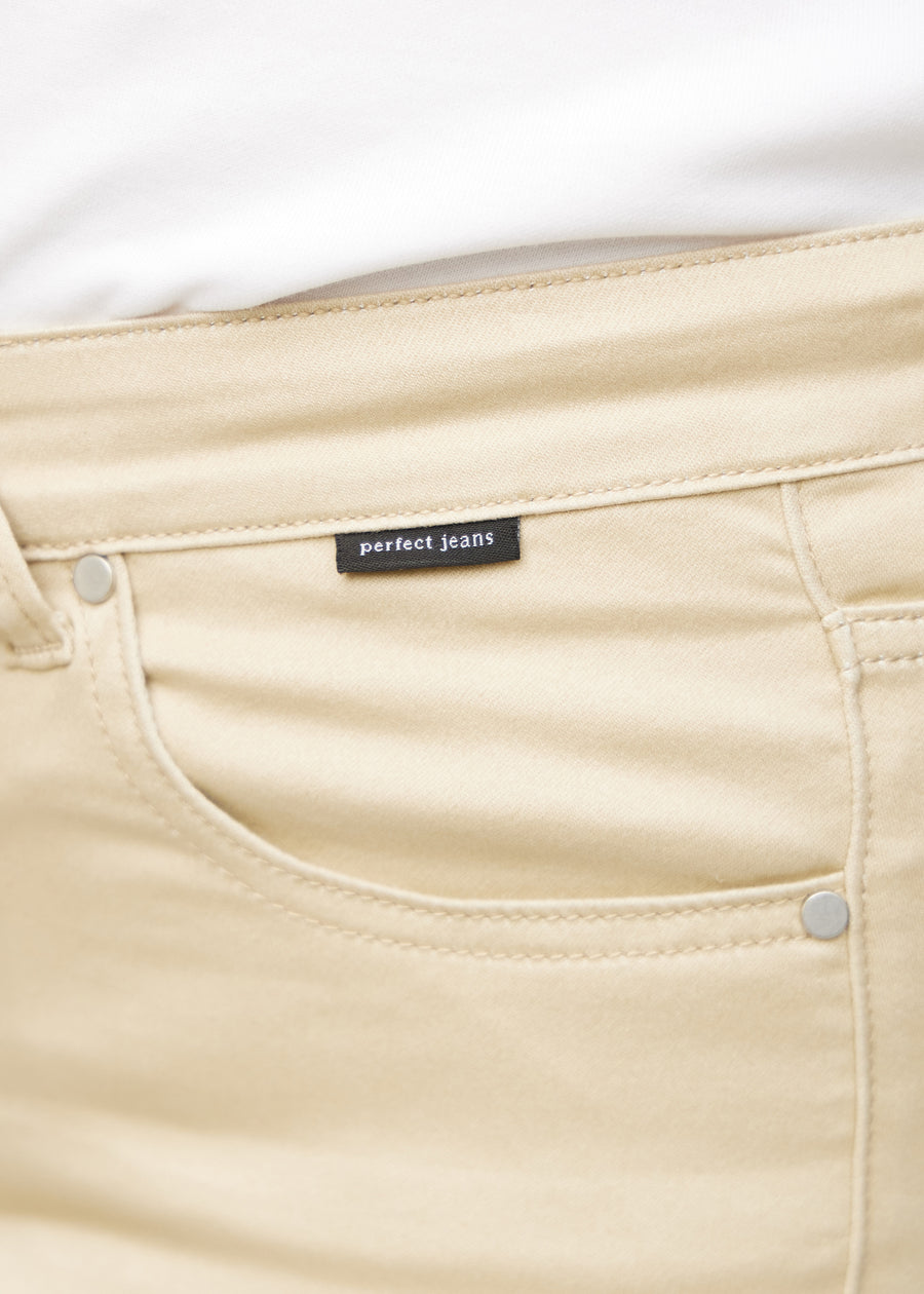 Close-up of beige jeans material with the Perfect Jeans logo label at the edge of the front pocket on a plus-size model.