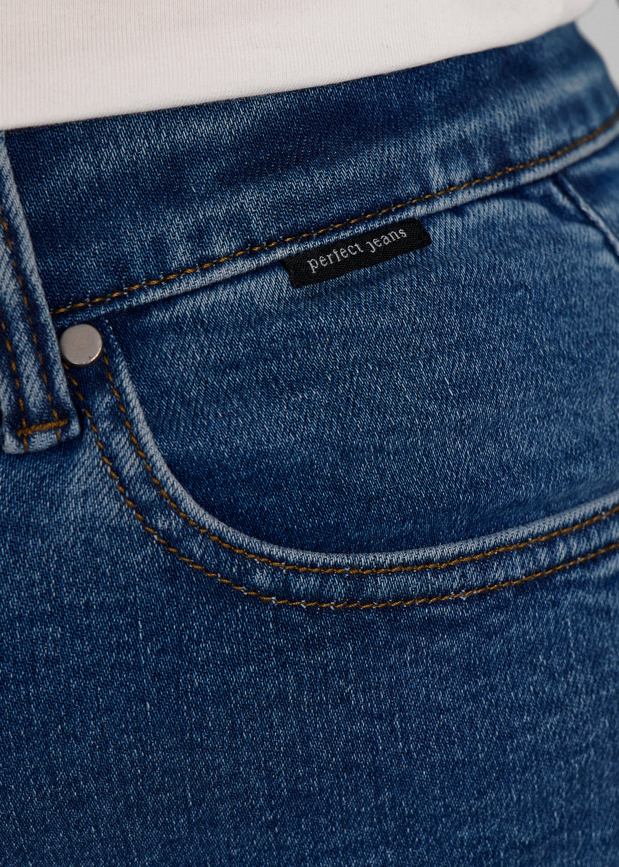 Nærbillede af mørkeblå denim med Perfect Jeans logoetiket ved forlommekanten, på en plus-size model.