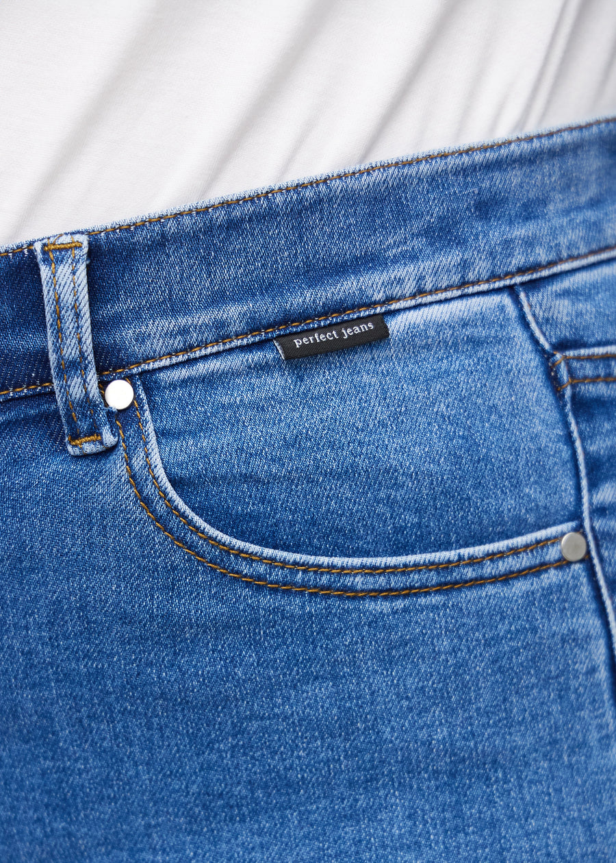 Close-up of blue denim with the Perfect Jeans logo label at the edge of the front pocket on a plus-size model.