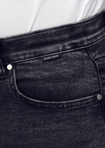 Nærbillede af mørkegrå denim med Perfect Jeans logoetiket ved forlommekanten, på en plus-size model.