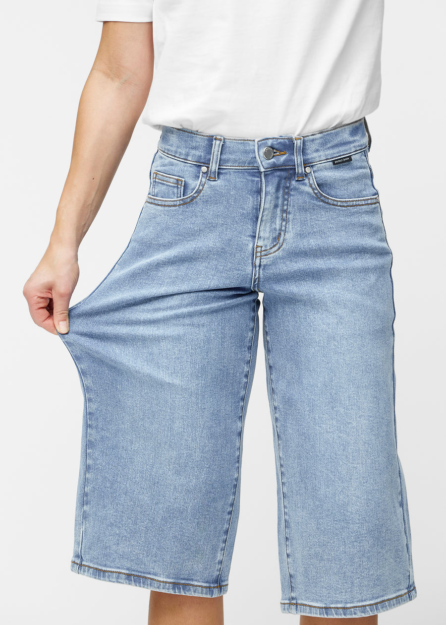 Model stretches the loose, light blue denim capris in the colour Waves at the hips to show the material’s stretch.