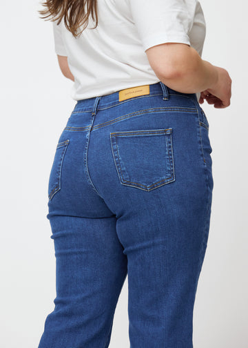 Dark blue mid-rise bootcut jeans in Oceans. Close-up back view on a plus-size model, showing the details.