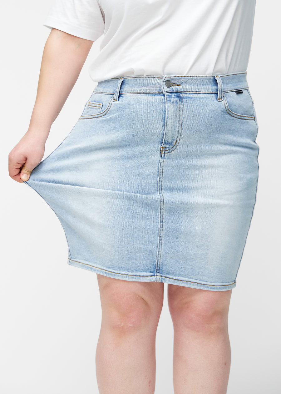 Plus-size model strækker lyseblå, tætsiddende og knælang denimnederdel ved låret for at vise stretch.