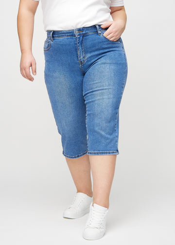 Denim regular capris, model name Rivers, with a straight fit through the leg and ending just below the knee on a plus-size model, seen from the front.