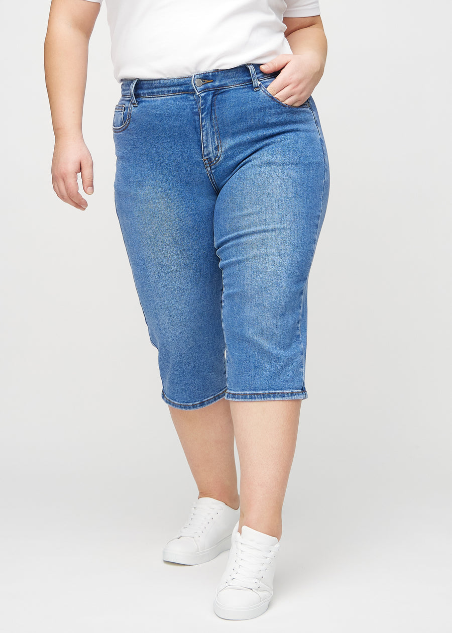 Denim regular capris, model name Rivers, with a straight fit through the leg and ending just below the knee on a plus-size model, seen from the front.