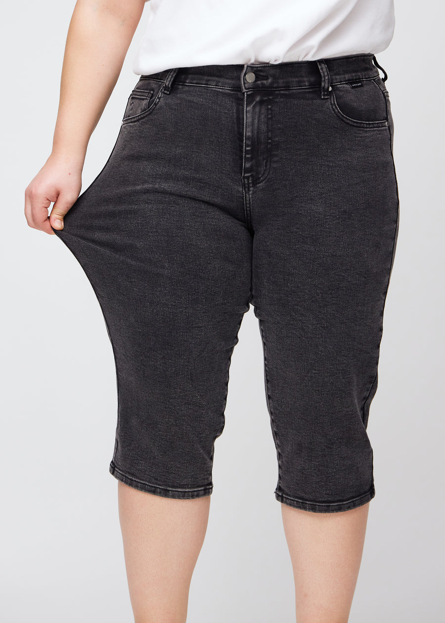The plus-size model stretches the capris at the thigh to show the stretch.