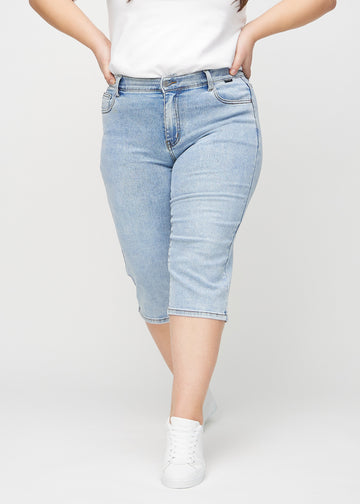 Light denim regular capris, style name Waves, with a straight fit through the leg and ending just below the knee on a plus-size model, seen from the front.