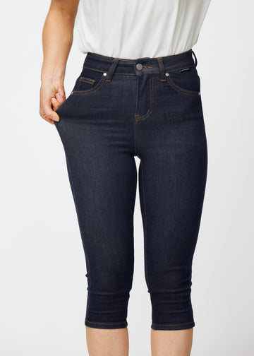 Model stretches deep dark blue denim capris for women in the colour Midnights at the thigh to show the material’s stretch.