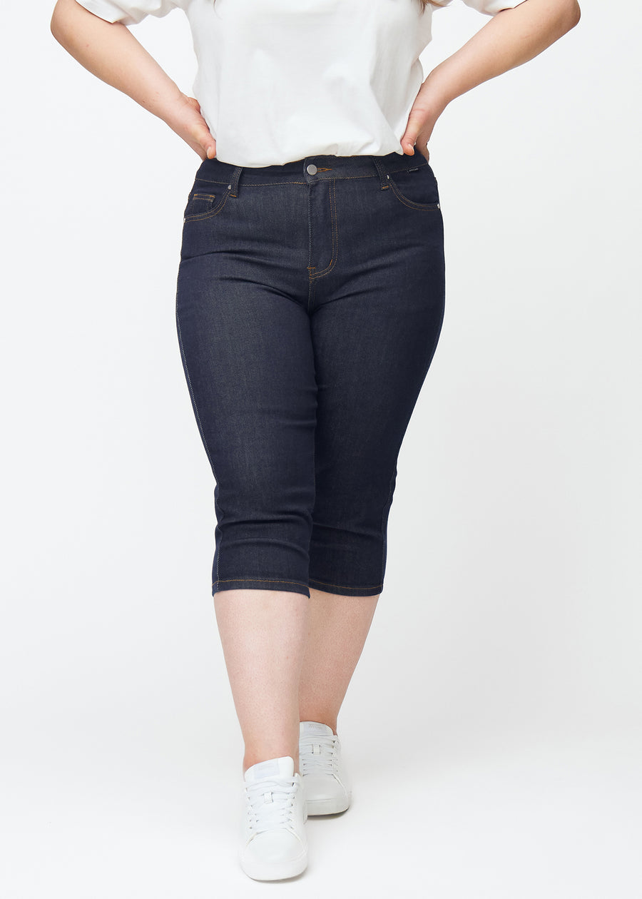 Deep dark blue denim capris for women in the colour Midnights with a skinny fit seen from the front on a plus-size model.