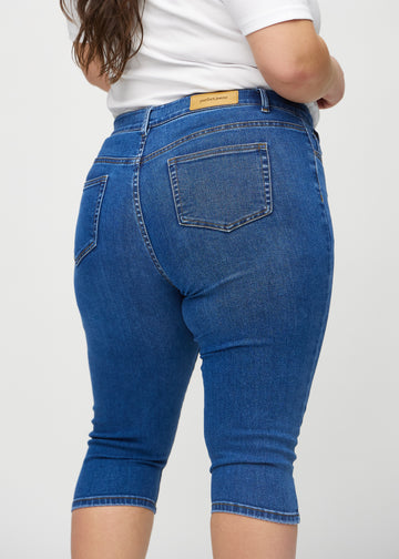 Skinny capris for women in dark blue denim, color Oceans. Close-up from behind on a plus-size model, highlighting pockets and stitching.