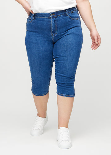 Skinny capris for women in dark blue denim, color Oceans. Front view on a plus-size model, showing the close-fitting legs ending just below the knee.
