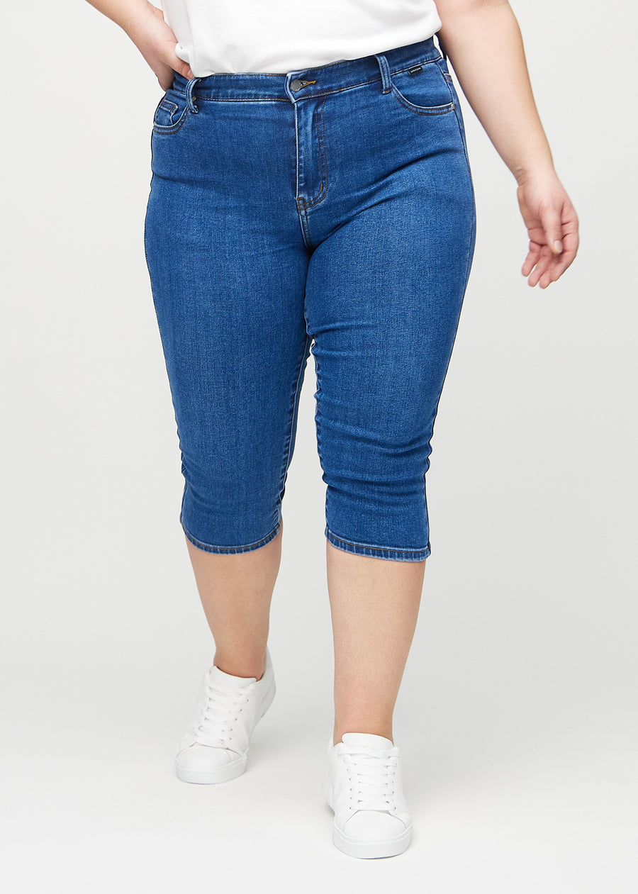Skinny capris for women in dark blue denim, color Oceans. Front view on a plus-size model, showing the close-fitting legs ending just below the knee.