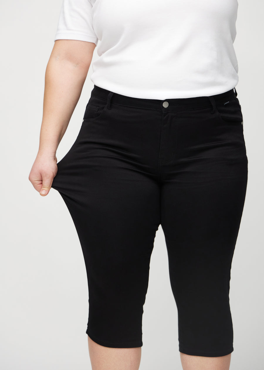Skinny capris for women in black fabric, color Ravens. A plus-size model stretches the fabric to demonstrate its flexibility.