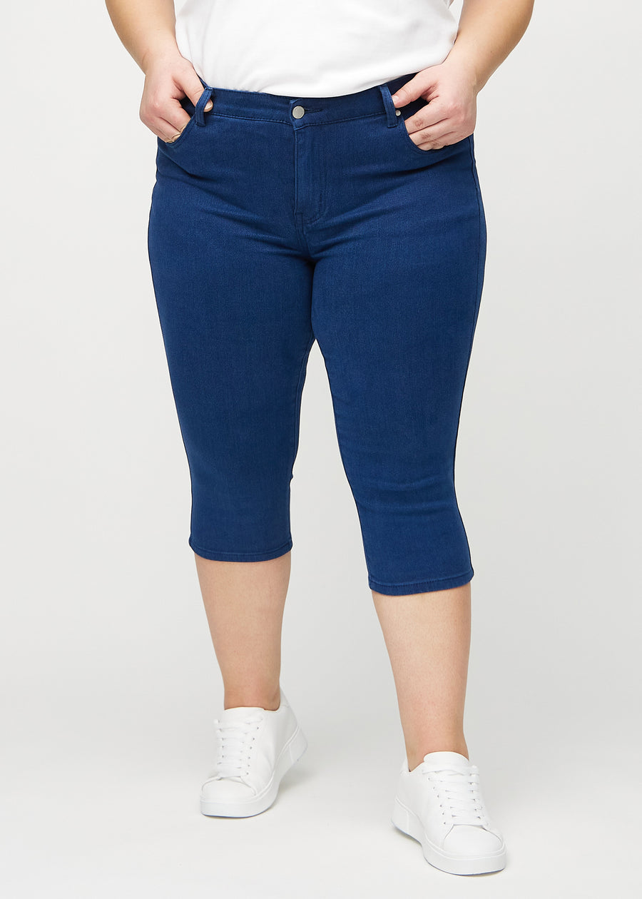 Dark blue skinny capris, model name Royals, which fit closely to the leg and end just below the knee on a plus-size model, seen from the front.