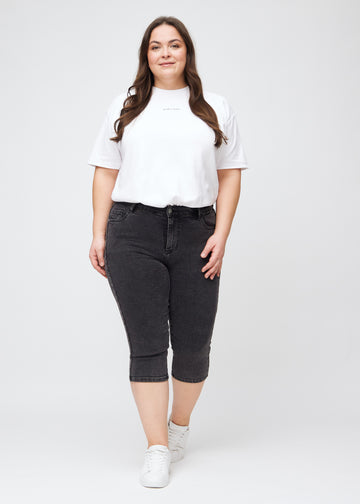 Skinny capris for women in dark grey denim, color Shadows. Full-length view of a plus-size model wearing the capris.