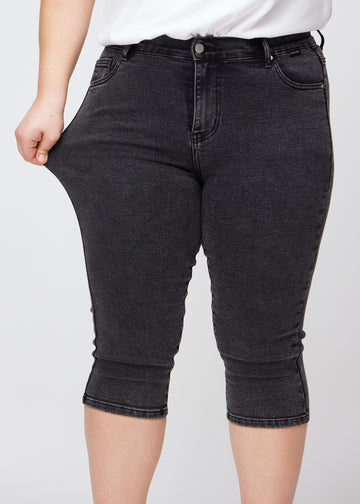 Skinny capris for women in dark grey denim, color Shadows. A plus-size model stretches the fabric to demonstrate its flexibility.