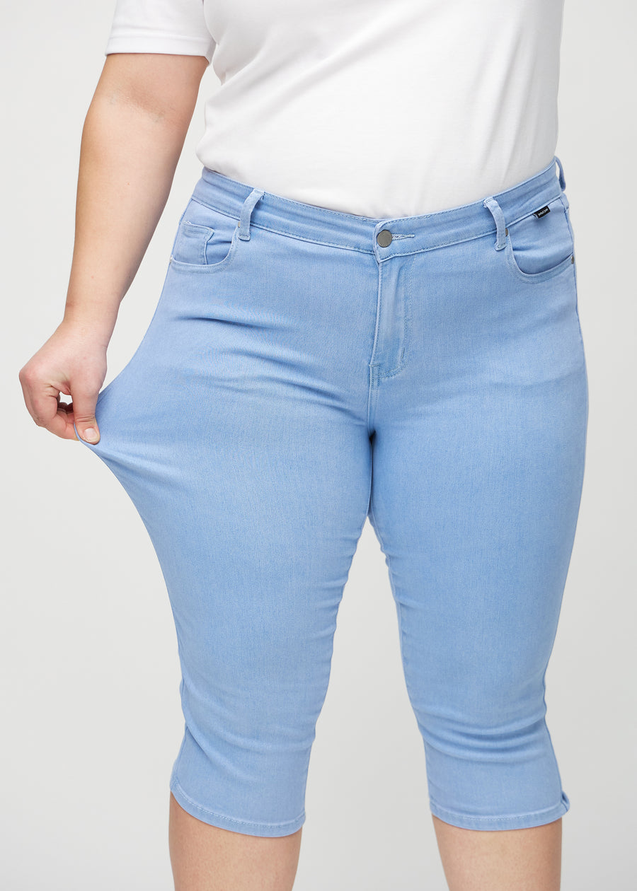 Skinny capris for women in light blue fabric, color Skies. A plus-size model stretches the fabric to demonstrate its flexibility.