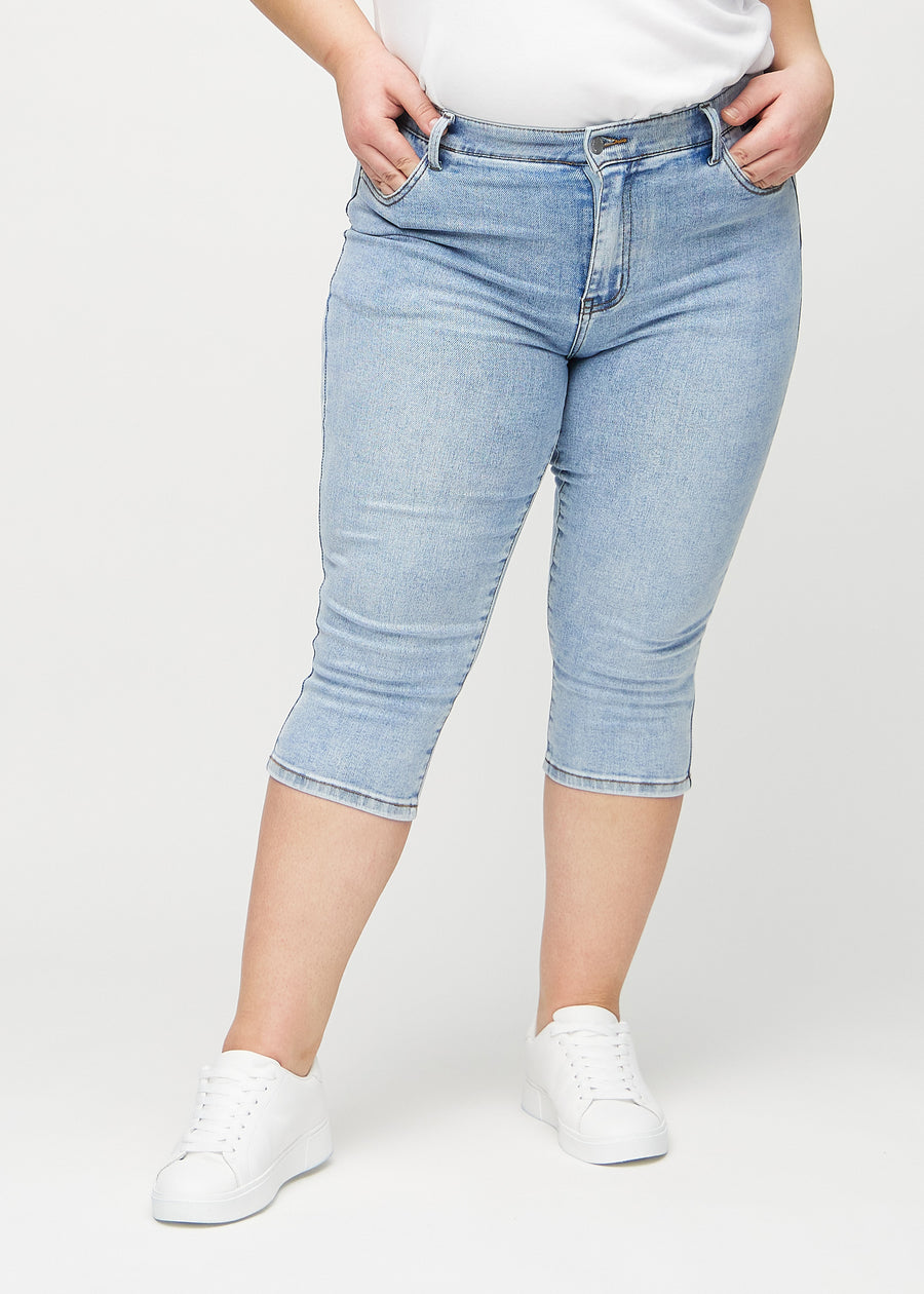 Skinny capris for women in light blue denim, color Waves. Front view on a plus-size model, showing the close-fitting legs ending just below the knee.