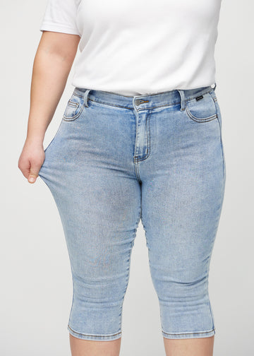 Skinny capris for women in light blue denim, color Waves. A plus-size model stretches the fabric to demonstrate its flexibility.