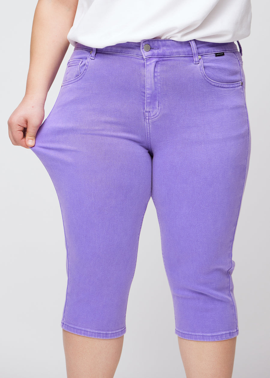 Slim capris for women in pastel purple jeans fabric, color Lavenders. A plus-size model pulls the fabric at the thigh to demonstrate stretch and flexibility.