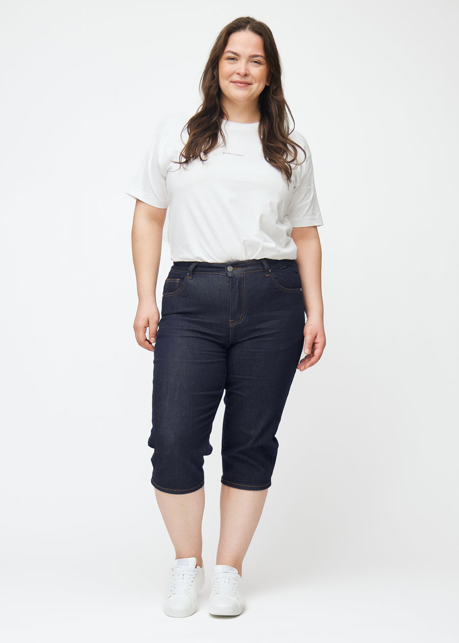 Full image of a plus-size model wearing deep dark blue denim capris for women in the colour Midnights with a slim fit.