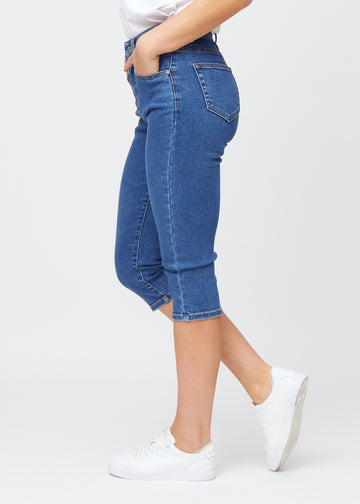 Slim capris for women in dark blue denim, color Oceans. Side view on a model, showing the tailored fit and mid-rise waist.