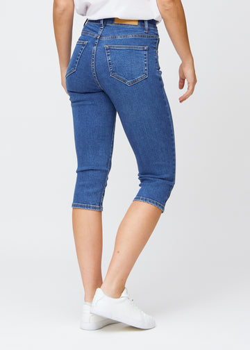 Slim capris for women in dark blue denim, color Oceans. Back view on a model, showing the fit, length and back pockets.