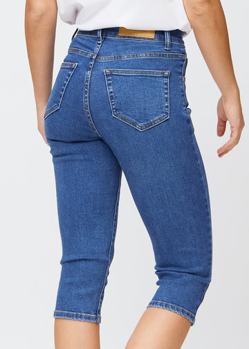 Slim capris for women in dark blue denim, color Oceans. Close-up from behind on a model, highlighting the back pockets and stitching.