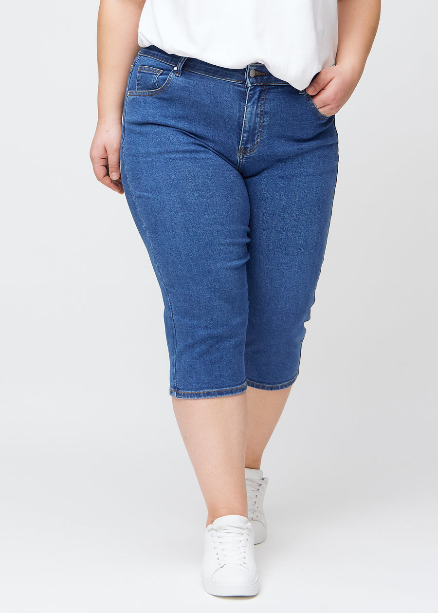 Slim capris for women in dark blue denim, color Oceans. Front view on a plus-size model, showing the fitted cut ending just below the knee.
