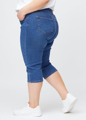 Slim capris for women in dark blue denim, color Oceans. Side view on a plus-size model, showing the tailored fit and mid-rise waist.