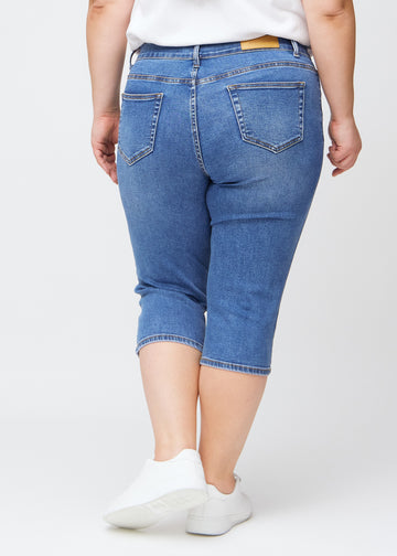 Slim capris for women in blue denim, color Rivers. Back view on a plus-size model, showing the fit, length and back pockets.