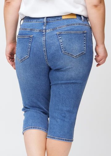 Slim capris for women in blue denim, color Rivers. Close-up from behind on a plus-size model, highlighting the back pockets and stitching.