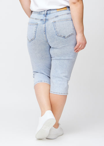 Slim capris for women in light blue denim, color Waves. Back view on a plus-size model, showing the fit, length and back pockets.