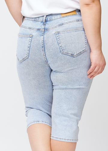 Slim capris for women in light blue denim, color Waves. Close-up from behind on a plus-size model, highlighting the back pockets and stitching.