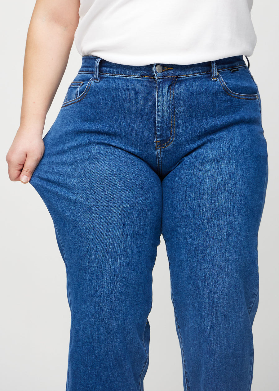 Loose jeans for women in dark blue, color Oceans. A plus-size model stretches the denim at the thigh to show the fabric&