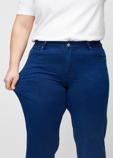 Regular jeans for women in dark blue, color Royals. A plus-size model stretches the fabric at the thigh to show its stretch.