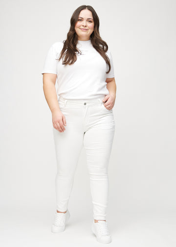 Skinny jeans for women in white, color Marguerites. Full-length view of a plus-size model in the jeans.