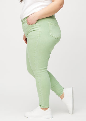 Light green skinny jeans seen from the side on a plus-size model.
