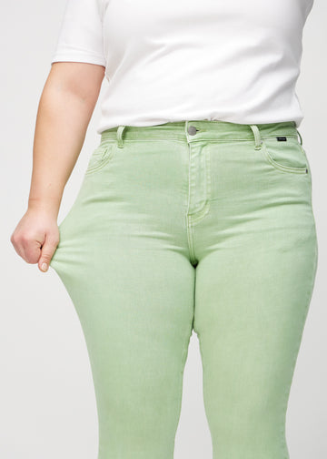 The plus-size model stretches the jeans at the thigh to show the stretch.