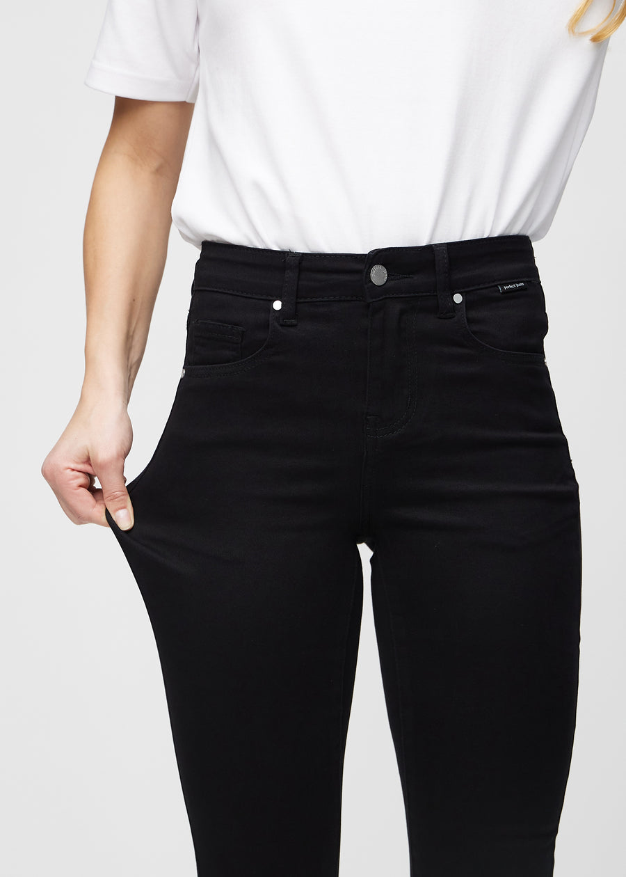 Skinny jeans for women in black, color Ravens. A model stretches the jeans at the thigh to show the fabric&