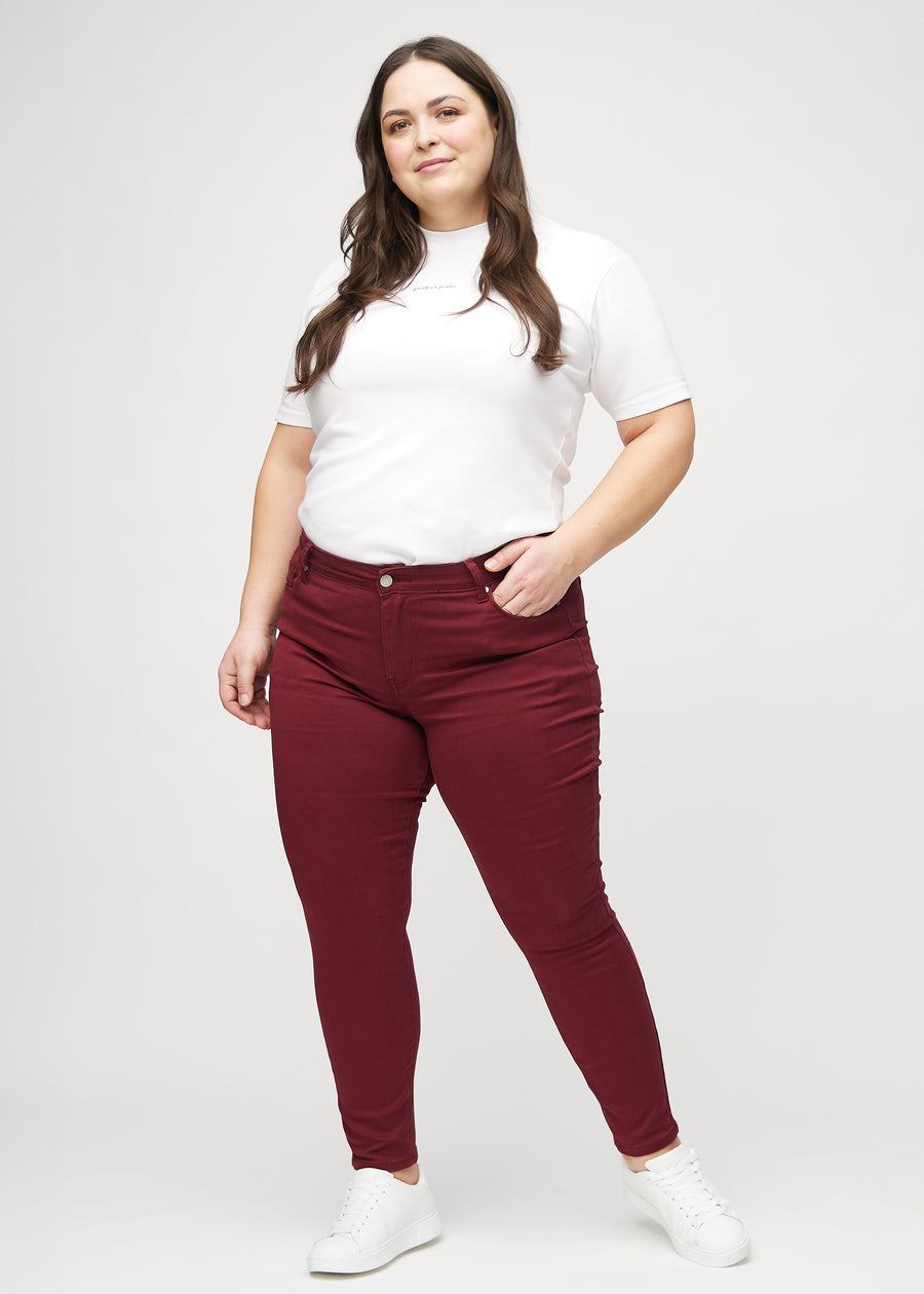Skinny jeans for women in dark red, color Santas. Full-length view of a plus-size model in the jeans.