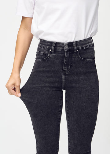 Skinny jeans for women in dark grey, color Shadows. A model stretches the jeans at the thigh to show the fabric&
