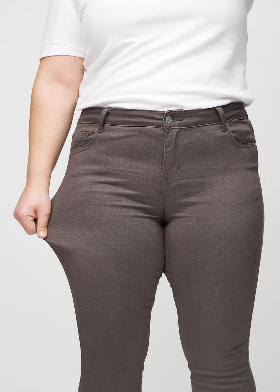 Skinny jeans for women in grey brown, color Thunders. A plus-size model stretches the jeans at the thigh to show the fabric&