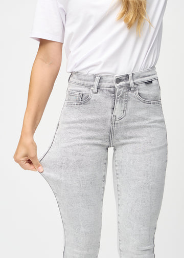 Slim jeans for women in light grey, color Ashes. A model stretches the jeans at the thigh to show the fabric&